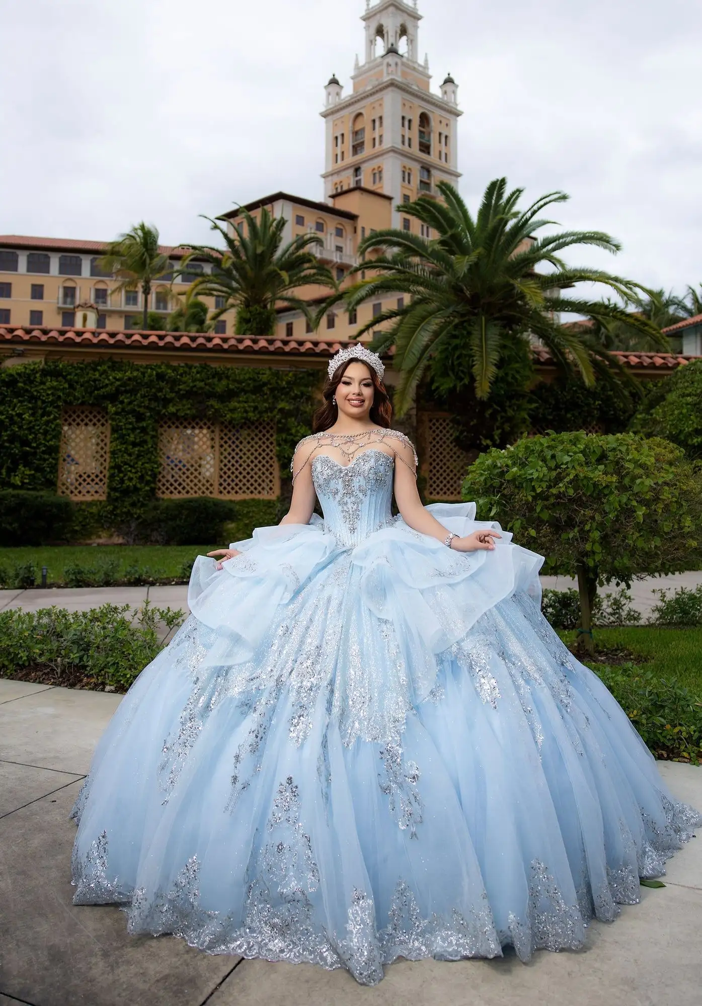 Morilee ice blue quinceañera ball gown with silver lace appliqué and a jeweled shoulder drape