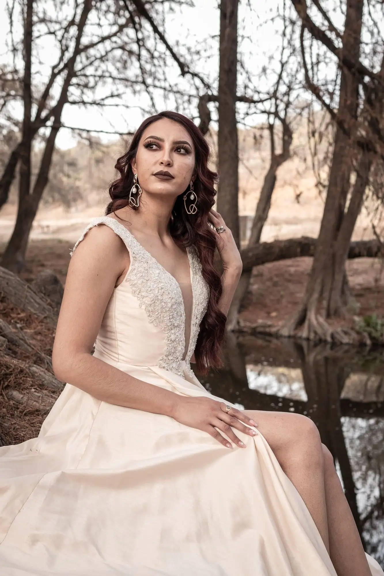 Champagne wedding gown with a deep-V lace bodice, seated beside a pond